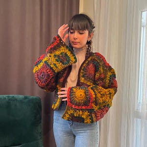 May include: A colorful crocheted cardigan with a brown base and multi-colored squares. The cardigan has long sleeves with bell-shaped cuffs and a loose fit.