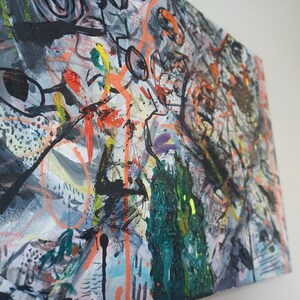 May include: Abstract painting on canvas with a mix of black, white, orange, green, and purple paint. The painting has a chaotic and energetic feel.