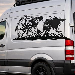 Puede incluir: Una furgoneta plateada con un gran adhesivo de vinilo negro en el panel lateral. El dise&ntilde;o gr&aacute;fico muestra una rosa de los vientos con las letras N y W, la silueta de un mapa mundial y una cordillera dentada en el borde inferior.