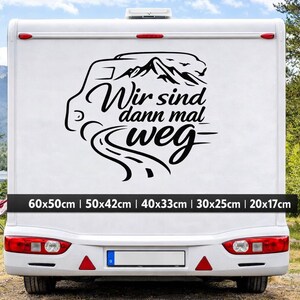 May include: A black vinyl decal applied to the rear of a white camper van. The design features a stylized camper van outline, mountain peaks, and a winding road, accompanied by the German text "Wir sind dann mal weg" in a cursive script.