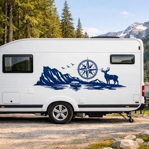 Puede incluir: Una caravana blanca con un gran adhesivo de vinilo azul oscuro en el lateral. El gr&aacute;fico muestra una cordillera, un peque&ntilde;o barco en el agua, una rosa de los vientos, tres p&aacute;jaros volando y la silueta de un ciervo de pie.