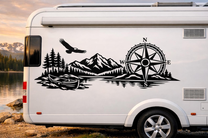 May include: A black vinyl decal applied to the side of a white recreational vehicle. The graphic features a mountain range, a forest of pine trees, a canoe on water, a flying eagle, and a large compass rose with the letters N, S, E, and W.