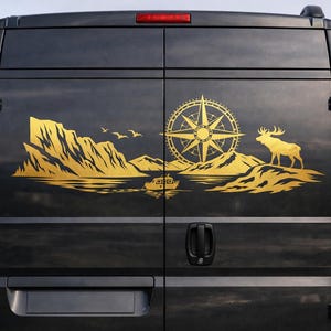 Puede incluir: Una furgoneta negra con un gran adhesivo dorado en las puertas traseras. El dise&ntilde;o muestra un paisaje monta&ntilde;oso, una rosa de los vientos, un peque&ntilde;o barco en el agua, la silueta de un p&aacute;jaro y un alce, todo en color dorado.