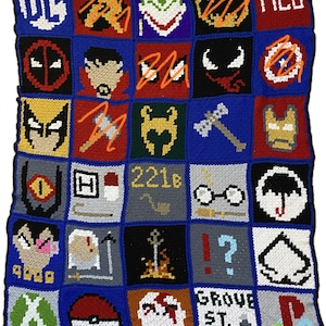 Op de afbeelding: Een gehaakt deken met een raster van kleurrijke vierkanten met verschillende popcultuuriconen, waaronder DC Comics, Marvel Comics en andere personages. Het deken is gemaakt met verschillende kleuren, waaronder rood, blauw, groen, geel en zwart.