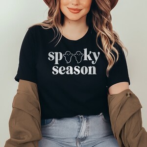 May include: A black t-shirt with a white graphic that says "spooky season" with three ghost silhouettes.