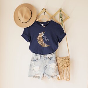 Puede incluir: Una camiseta azul marino con un gr&aacute;fico de luna creciente hecho de flores y el texto "Stay Wild".