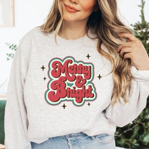 May include: A grey sweatshirt with a red and green retro-style graphic that says "Merry & Bright".