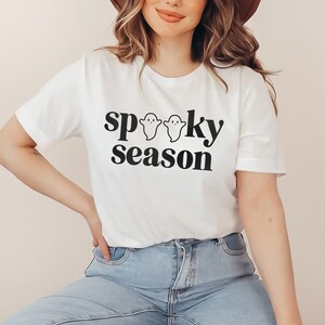 May include: White t-shirt with black text that reads "spooky season" and three small ghost illustrations.
