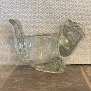 May include: A clear glass squirrel shaped dish. The dish is shaped like a squirrel sitting on its haunches with its tail curled around its back.