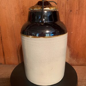 May include: A brown and white ceramic jar with a metal lid and handle. The jar has a crackled glaze and is in good condition.
