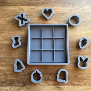 May include: A gray silicone baking mat with a grid pattern and nine cut-out shapes: a heart, a stocking, a Christmas tree, a pumpkin, a ghost, a strawberry, a bunny, a circle, and an X.