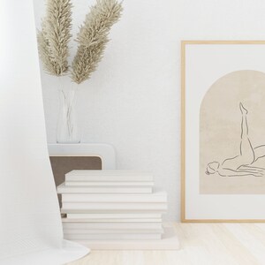 K&ouml;nnte beinhalten: Ein gerahmter Druck einer Linienzeichnung einer Person, die eine Yoga-Pose in einem Torbogen auf beigefarbenem Hintergrund macht. Der Rahmen ist aus hellem Holz und der Druck h&auml;ngt an einer wei&szlig;en Wand.