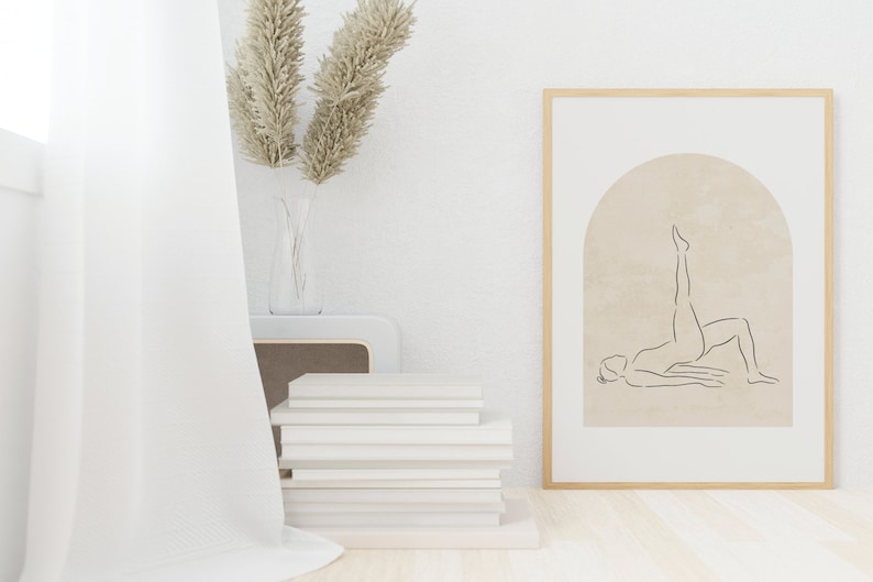 K&ouml;nnte beinhalten: Ein gerahmter Druck einer Linienzeichnung einer Person, die eine Yoga-Pose in einem Torbogen auf beigefarbenem Hintergrund macht. Der Rahmen ist aus hellem Holz und der Druck h&auml;ngt an einer wei&szlig;en Wand.