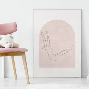K&ouml;nnte beinhalten: Ein gerahmter Druck eines Strichm&auml;nnchens, das eine Yoga-Pose vor einem rosafarbenen Bogen macht. Der Druck h&auml;ngt an einer wei&szlig;en Wand.