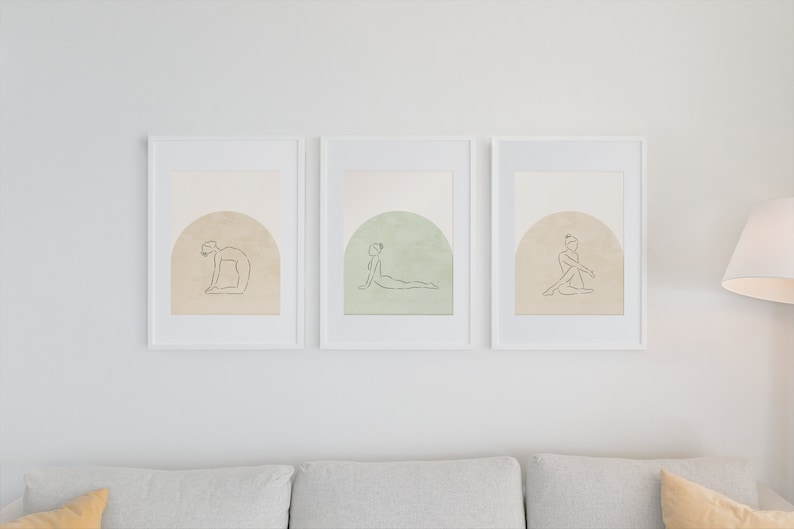May include: Three white framed prints with minimalist line drawings of people in yoga poses on a beige background. Each print features a different pose and a subtle color gradient in the background.