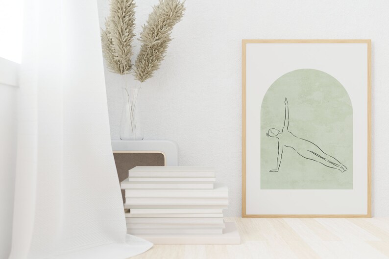 May include: A framed print with a minimalist line drawing of a person doing a side plank exercise. The drawing is on a light green background with a textured arch shape. The frame is light wood.
