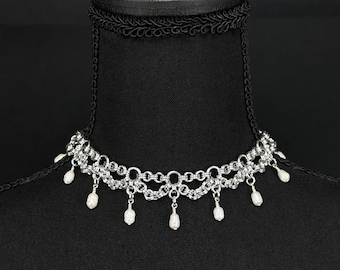 May include: A silver chain necklace with a delicate design and pearl accents. The necklace is displayed on a black mannequin bust.