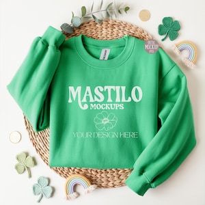 Green Gildan 18000 folded sweatshirt mockup styled with soft shamrock props, perfect for showcasing St. Patrick’s Day or everyday apparel designs in a clean flat-lay layout.