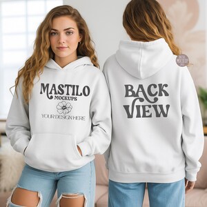May include: Two white hoodies, front and back views. The front hoodie displays "MASTILO MOCKUPS", a flower graphic, and "YOUR DESIGN HERE". The back hoodie features "BACK VIEW" in grey text. Both have a front pocket and a hood.