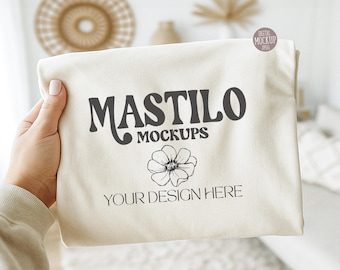 May include: A cream-coloured fabric displays the text "MASTILO MOCKUPS" in dark grey, a floral graphic, and the words "YOUR DESIGN HERE." A small, round sticker in the top right corner reads "DIGITAL MOCKUP JPEG."