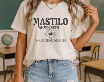 May include: Cream-colored t-shirt with the text "MASTILO MOCKUPS" above a floral design and "YOUR DESIGN HERE" below. The model is wearing denim shorts. The shirt is a mockup for design placement.
