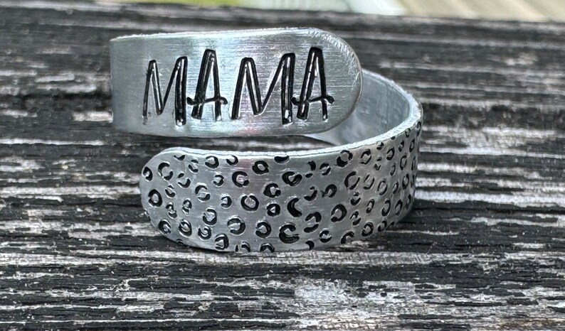 May include: A silver metal bracelet with a leopard print design and the word "MAMA" engraved on the top.
