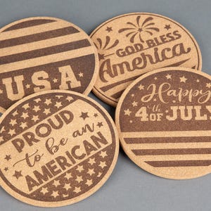 May include: Four round cork coasters with patriotic designs. One says "USA" with stripes, another says "God Bless America" with fireworks, a third says "Proud to be an American", and the last says "Happy 4th of July".