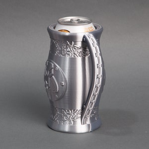 K&ouml;nnte beinhalten: Ein silberner Metall-Getr&auml;nkedosenhalter mit einem komplizierten Design und einem Griff. Der Halter ist f&uuml;r eine Standard-Getr&auml;nkedose ausgelegt.