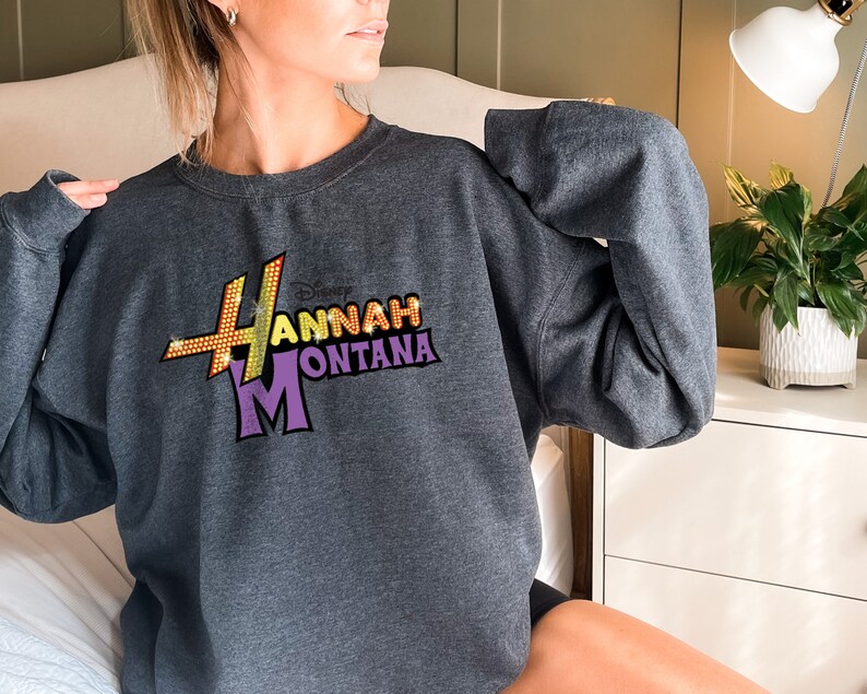 Puede incluir: Una sudadera gris con un gr&aacute;fico brillante de color morado, amarillo y naranja del programa de Disney Channel "Hannah Montana".
