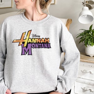 Puede incluir: Sudadera gris con un estampado gr&aacute;fico morado y amarillo que dice "Disney Hannah Montana".