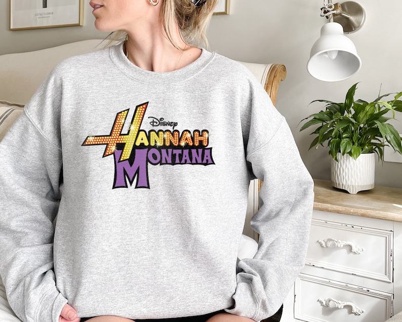 Puede incluir: Sudadera gris con un estampado gr&aacute;fico morado y amarillo que dice "Disney Hannah Montana".