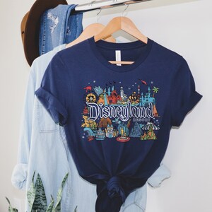 Puede incluir: Una camiseta azul marino con un gr&aacute;fico colorido de iconos de Disneyland Resort, incluyendo el Castillo de la Bella Durmiente, Space Mountain y el Matterhorn. El texto "Disneyland Resort" est&aacute; impreso en blanco.