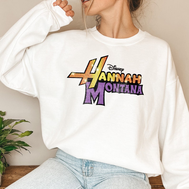 Puede incluir: Sudadera blanca con un estampado gr&aacute;fico morado y amarillo del programa de Disney Channel "Hannah Montana".