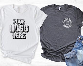 May include: Two t-shirts, one white and one dark grey. The white t-shirt has the text "YOUR LOGO HERE" in a bold, blocky font. The grey t-shirt has a circular design with the text "CUSTOM SHIRT YOUR LOGO HERE POCKET SIZE".