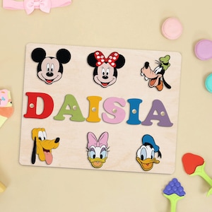 May include: A wooden puzzle with colorful letters spelling out the name "DAISIA". The puzzle features various Disney characters, including Mickey Mouse, Minnie Mouse, Donald Duck, and Goofy.