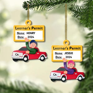 May include: Two Christmas ornaments shaped like learner's permits, each with a name and the date 2024. One features a red car with a person waving. The other ornament also has a red car with a person waving.