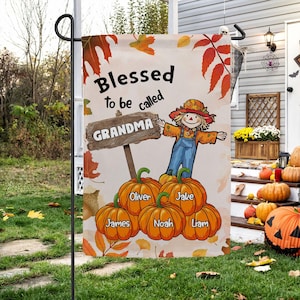 Könnte beinhalten: Eine Gartenflagge zum Thema Herbst mit dem Text "Blessed to be called Grandma". Die Flagge zeigt eine Illustration einer Vogelscheuche, die ein Schild mit der Aufschrift "GRANDMA" über Kürbissen mit Namen hält. Herbstblätter schmücken den Hintergrund.