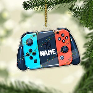 May include: A blue and red Nintendo Switch controller Christmas ornament with a string of lights and the word "NAME" in the center.