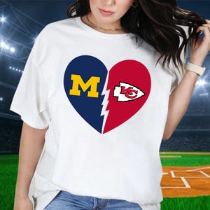 Könnte beinhalten: Weißes T-Shirt mit einem Herzdesign, das in zwei Hälften geteilt ist. Eine Hälfte ist marineblau mit einem gelben "M", die andere ist rot mit einem weißen Pfeil-Logo. Das Design wird durch einen weißen Blitz geteilt.