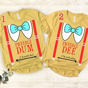 May include: Two yellow t-shirts with red suspenders and a blue bow tie. The text on the shirts reads "TWEEDLE DUM (I'm with dee)" and "TWEEDLE DEE (I'm with dum)".