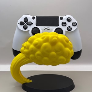 Puede incluir: Un mando de PlayStation 4 blanco se encuentra en un soporte en forma de nube amarilla. El soporte tiene una base negra.