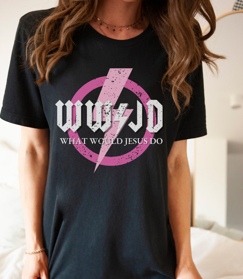 May include: Black t-shirt featuring the text "WWJD" in a white, gothic-style font, with a pink lightning bolt and a pink circle. Below the text is "WHAT WOULD JESUS DO" in a sans-serif font.