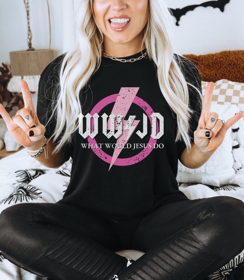 May include: Black t-shirt featuring a pink circle with a lightning bolt and the text "WWJD WHAT WOULD JESUS DO" in a distressed white font. The shirt is a casual style.