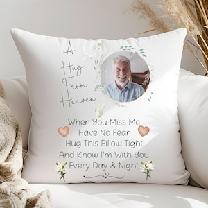 May include: White throw pillow featuring a photograph of a man within a circular frame adorned with green foliage and white blossoms. The text "A Hug From Heaven" is positioned above the image, while the words "When You Miss Me Have No Fear Hug This Pillow Tight And Know I'm With You Every Day & Night" are displayed beneath.