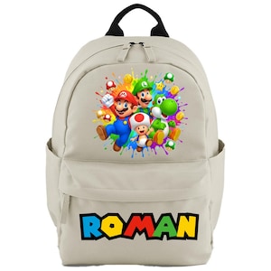 May include: A beige backpack with a vibrant graphic of Mario, Luigi, Yoshi, and Toad, with paint splashes. The name "ROMAN" is written in colourful block letters at the bottom. It has a black handle and two side pockets.