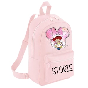 May include: A pale pink backpack with a front pocket and adjustable straps. The backpack features a graphic of Jessie from Toy Story inside a Minnie Mouse-shaped design. The word "STORIE" is printed on the front pocket.