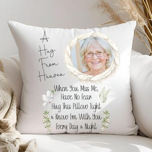May include: A white square throw pillow featuring a circular photo of an older person with glasses framed by a feather wreath. The text reads A Hug From Heaven and When You Miss Me, Have No Fear, Hug This Pillow Tight & Know I'm With You Every Day & Night, accompanied by illustrations of white doves and small flowers.