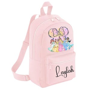 May include: Pink backpack featuring a colourful Disney princess design and a bow. The backpack has a zipped pocket and the name "Laylah" is printed on the front.