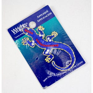 May include: A blue iron-on appliqué of a lizard with red and white detailing, packaged on a blue and white card. The card features the Wrights logo and the words "Appliqué" and "Iron Ons".