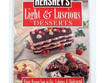 Puede incluir: Portada de libro de cocina con el logo de Hershey's y el título "Light & Luscious Desserts". La imagen muestra una tarta de chocolate en capas con glaseado rosa y fresas, además de otros postres. También se ve el texto "Every Recipe Low in Fat, Calories & Cholesterol".